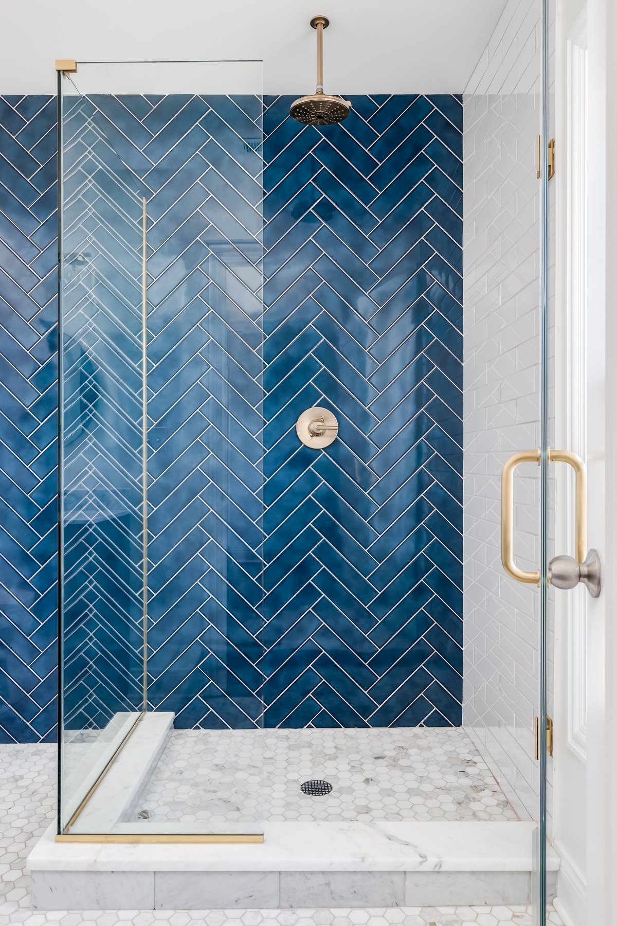 Blue herringbone tile shower wall with gold hardware, modern luxury tile installation.