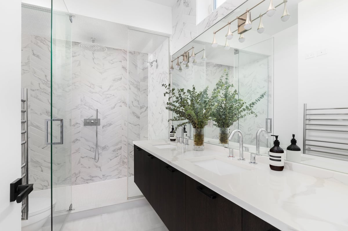A beautiful bathroom with a floating dark wood cabinet, marble countertop and a herringbone tiled walk-in shower