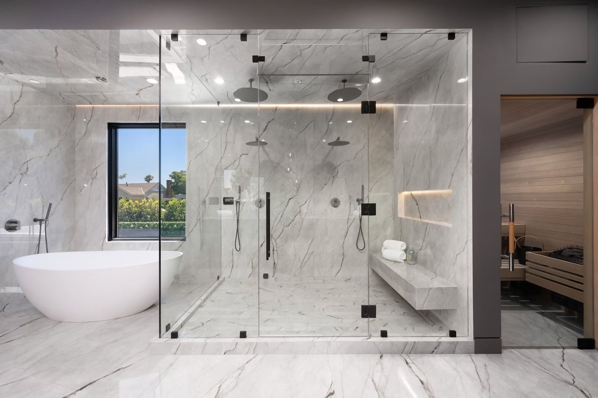 Modern luxury bathroom with a large glass shower, freestanding tub and sauna, featuring marble walls and floors