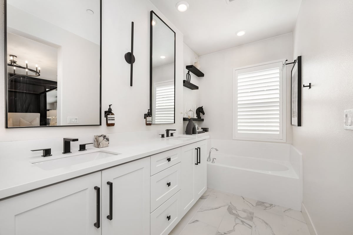 Modern bathroom with white cabinets, black fixtures and a bathtub under a window