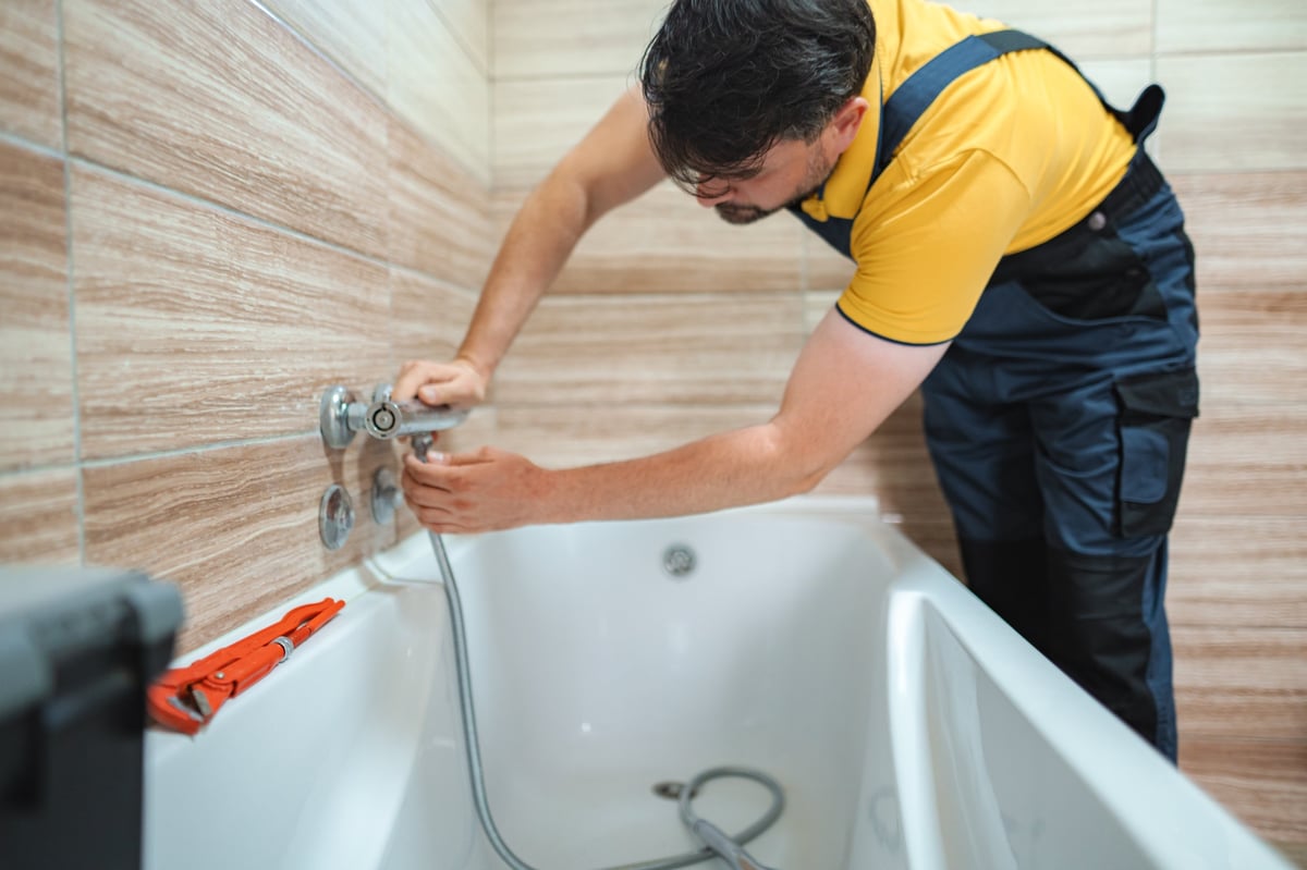 Plumber working on a new bathtub installation, connecting the flexible hose to the faucet