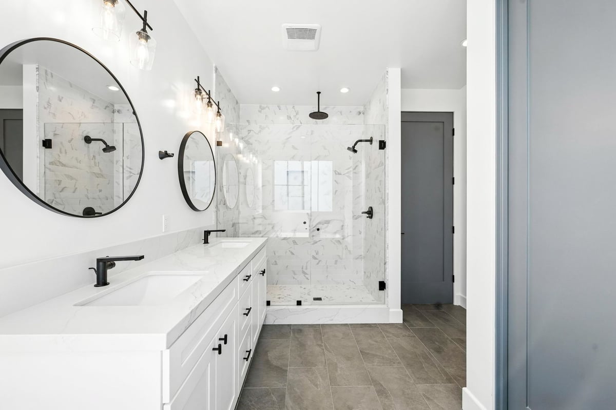 A sleek modern bathroom with a double vanity, large soaking tub and circular mirrors with black fixtures