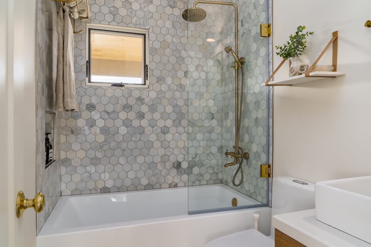 Modern bathroom in white with shower tub, hexagonal tile and gold brass fixtures