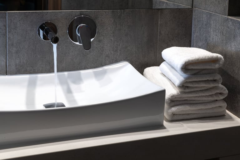 Modern chrome bathroom faucet and sink in contemporary dark tile setting.
