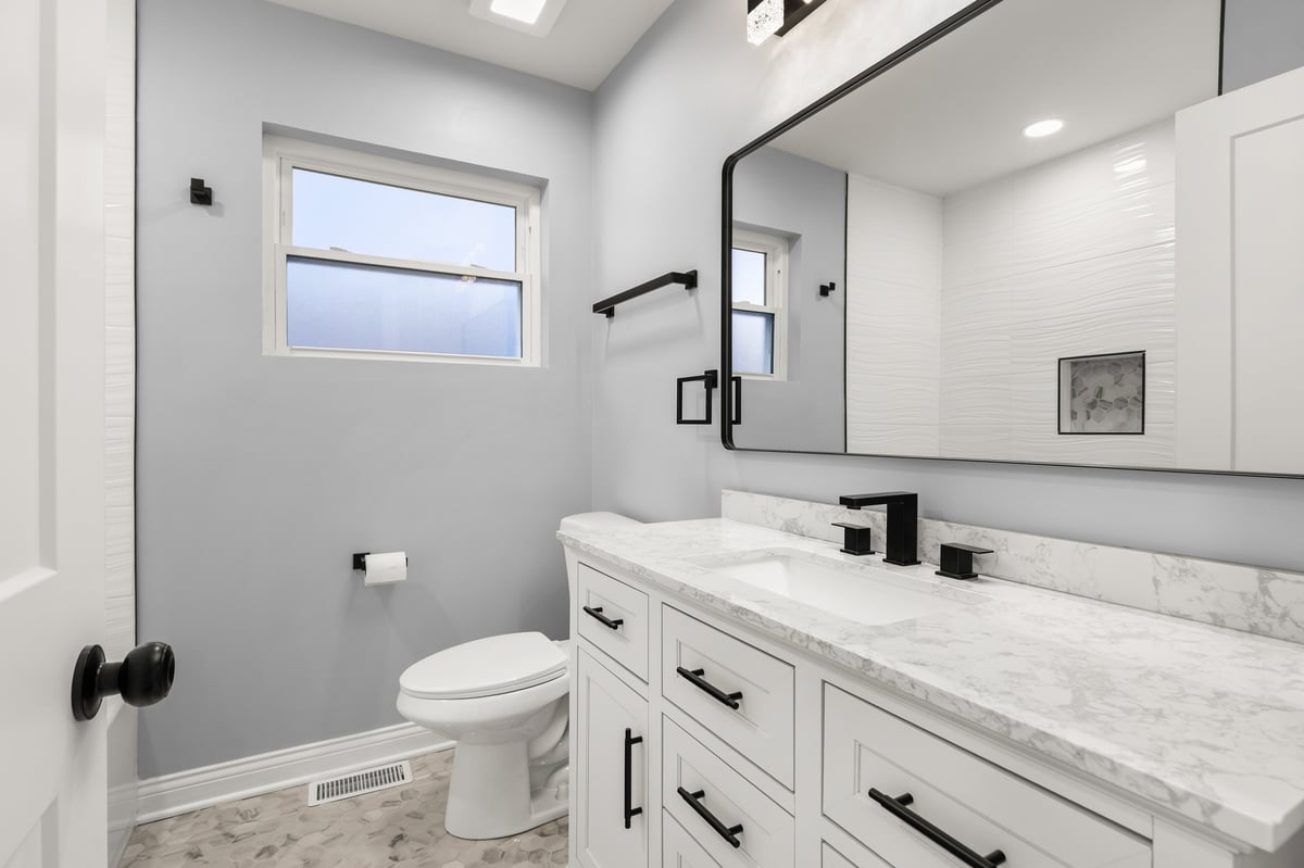 A modern white bathroom featuring a white vanity with a marble countertop and hexagon tile floor