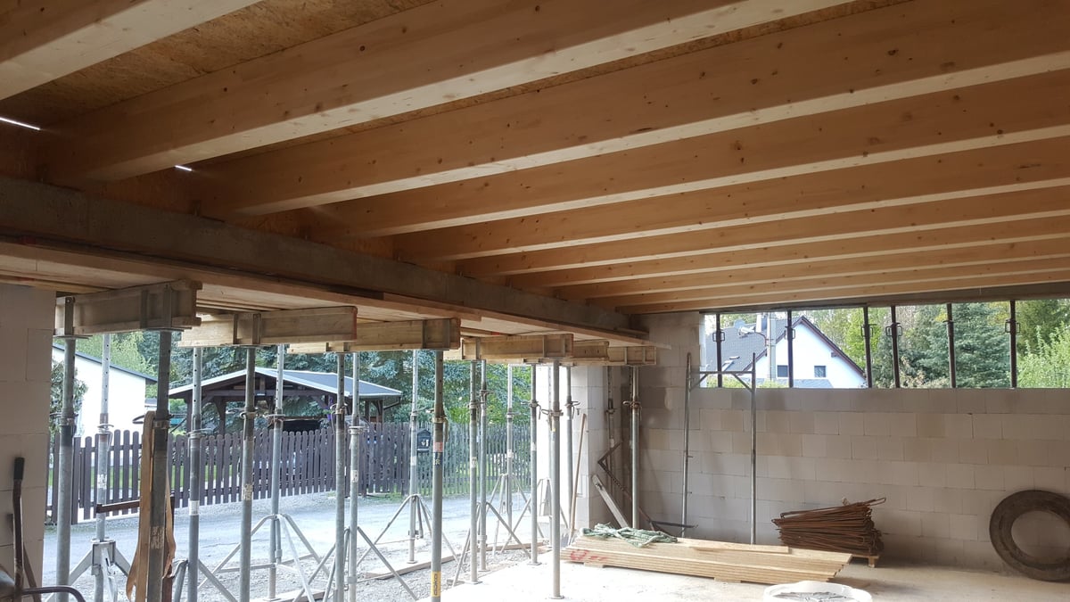Wooden beams and OSB panels are installed for a new floor, supported by adjustable metal props and scaffolding during construction