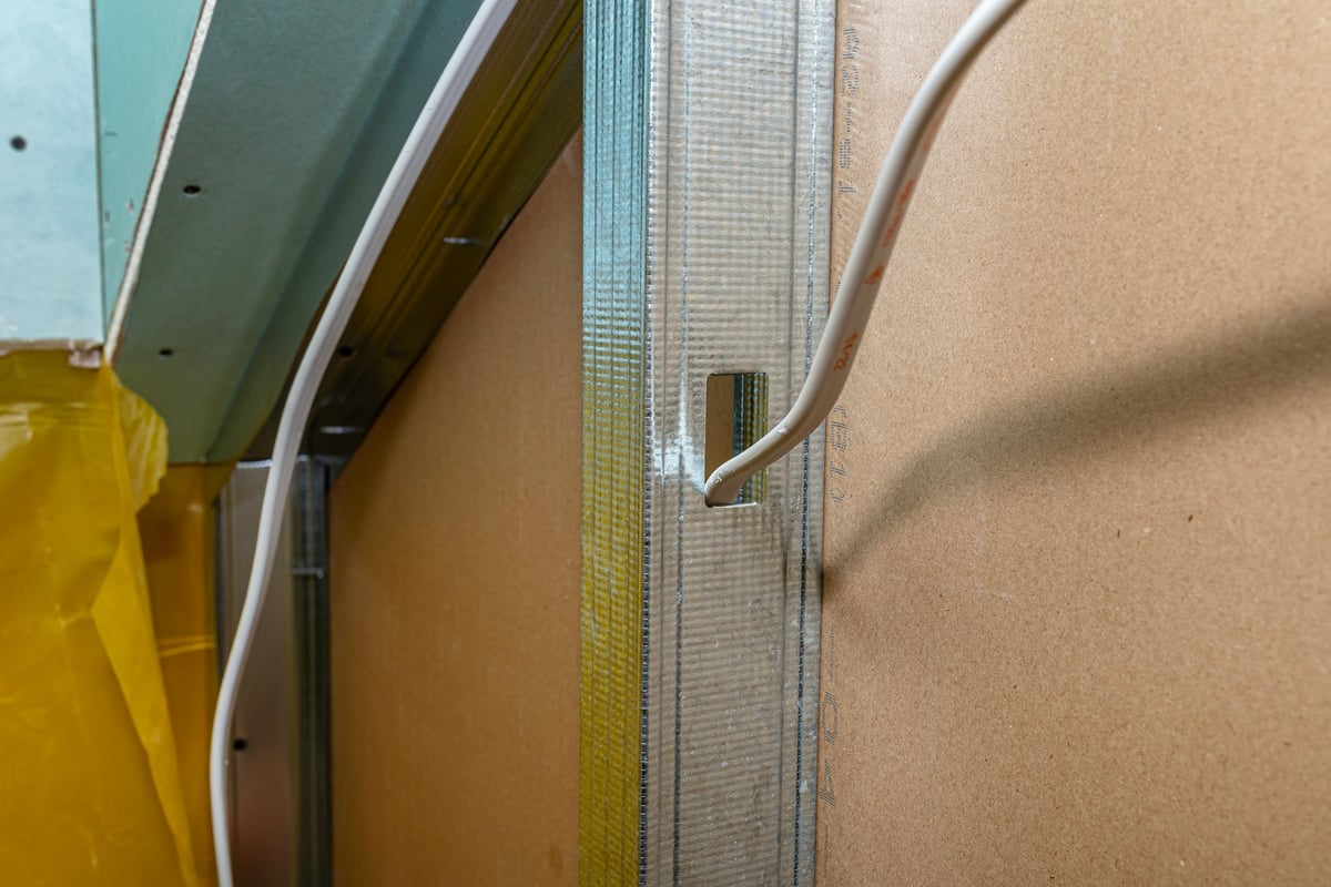Drywall construction featuring metal profiles, plasterboard, electrical cables, and a yellow vapor barrier