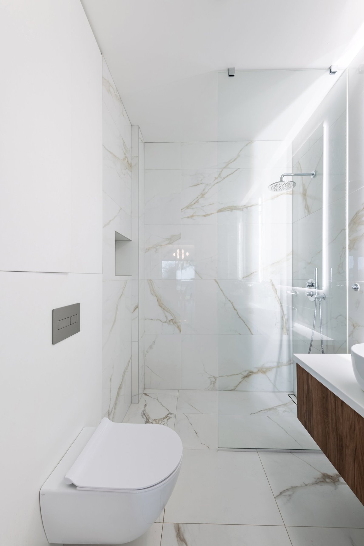 Bright modern bathroom with white marble tiles, frameless walk-in glass shower and floating wood vanity