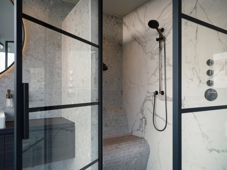 Modern walk-in shower with frameless glass, marble walls, and rainfall showerhead.