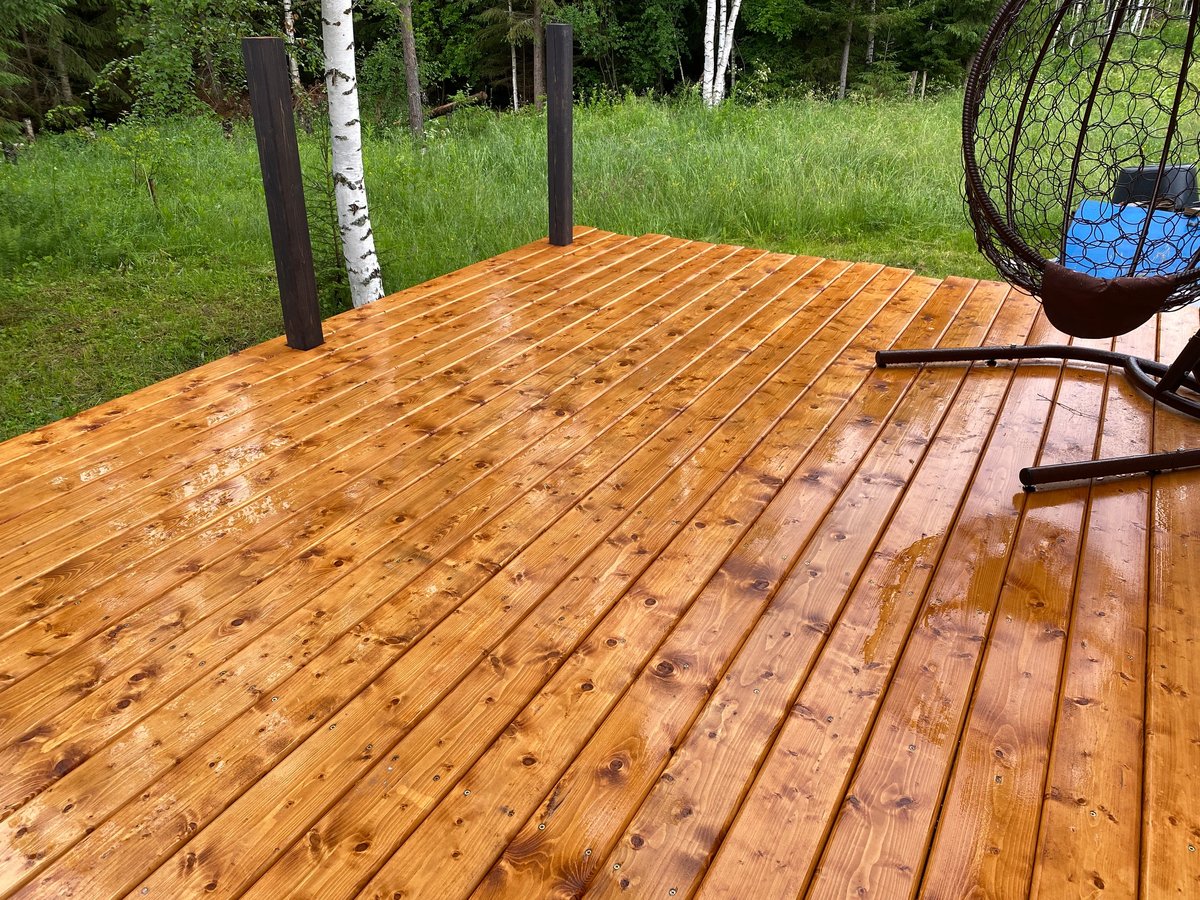 New wooden terrace with freshly treated deck boards after rain. Outdoor decking under construction surrounded by forest, showcasing home improvement, craftsmanship and modern exterior living