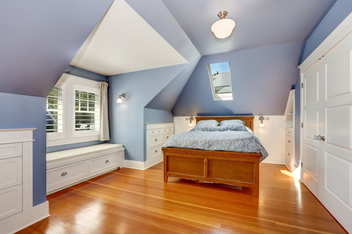 Lavender interior of attic bedroom with queen size bed and hardwood floor. Also window seat and built-in cabinets. Northwest, USA