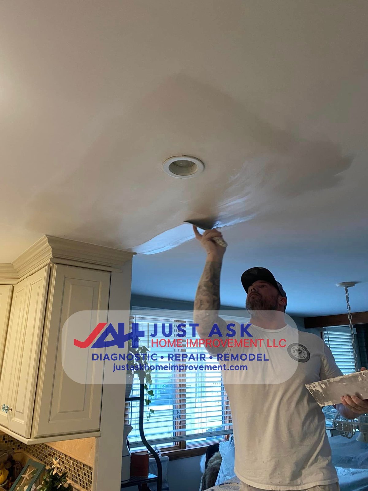 Just Ask Home Improvement crew member applying joint compound to a ceiling drywall repair with a taping knife