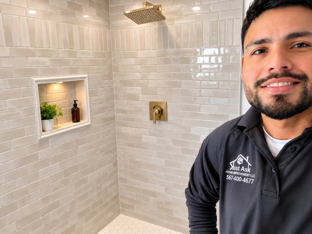 Just Ask Home Improvement crew member in a dark polo shirt standing in a finished bathroom with white subway tile shower, recessed niche and brass fixtures