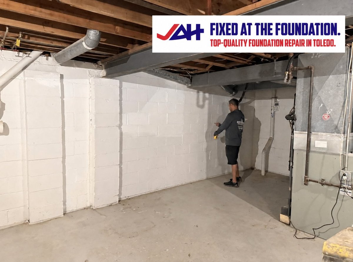 Basement foundation repair in progress with worker applying white sealant to concrete walls, featuring A+ Plus logo and text for Toledo foundation repair services.