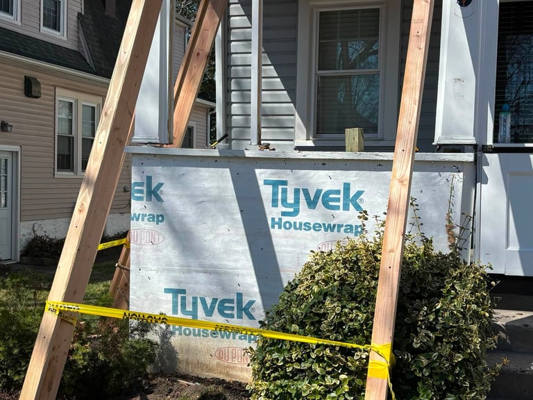 House exterior under structural repair with exposed wood framing, housewrap sheathing and yellow caution tape in front