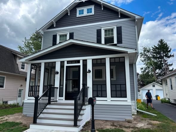Dark gray two-story house with white trim and a front porch entry with black doors under a blue sky