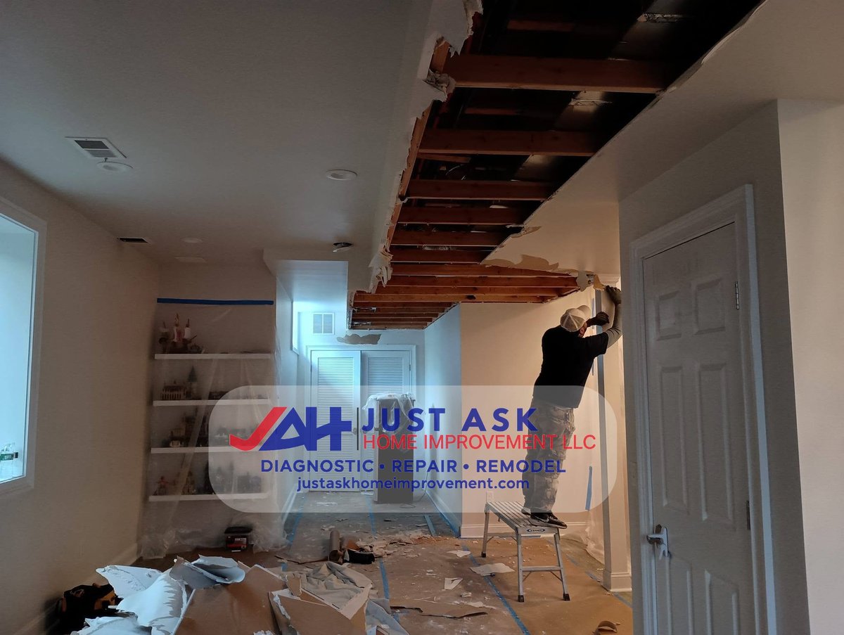 Crew member on a ladder inspecting exposed ceiling framing before new drywall is installed