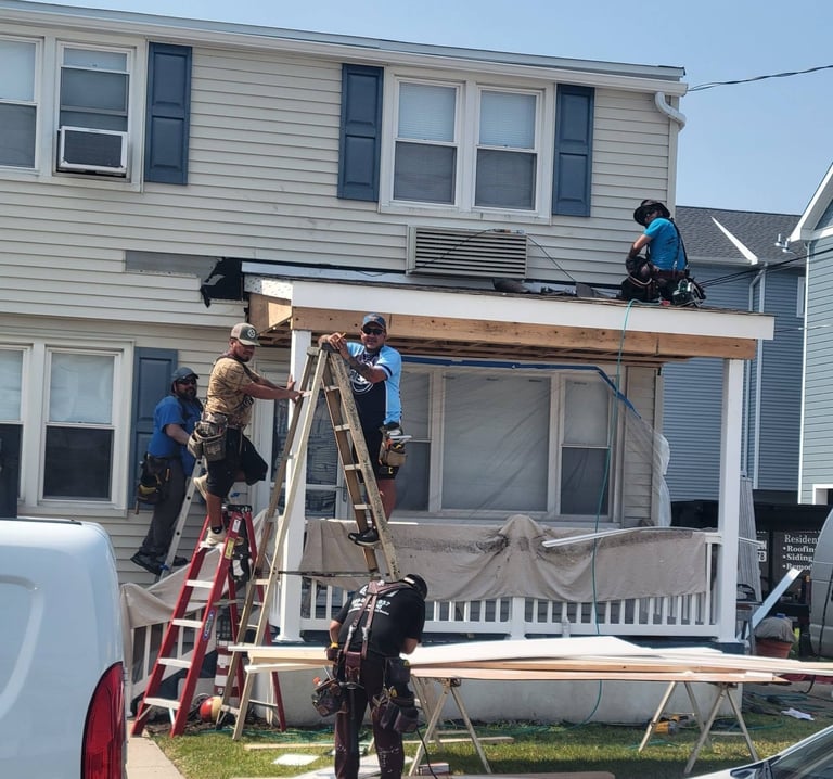 Two workers on ladders and scaffolding installing a large exterior window opening on a two-story residential house